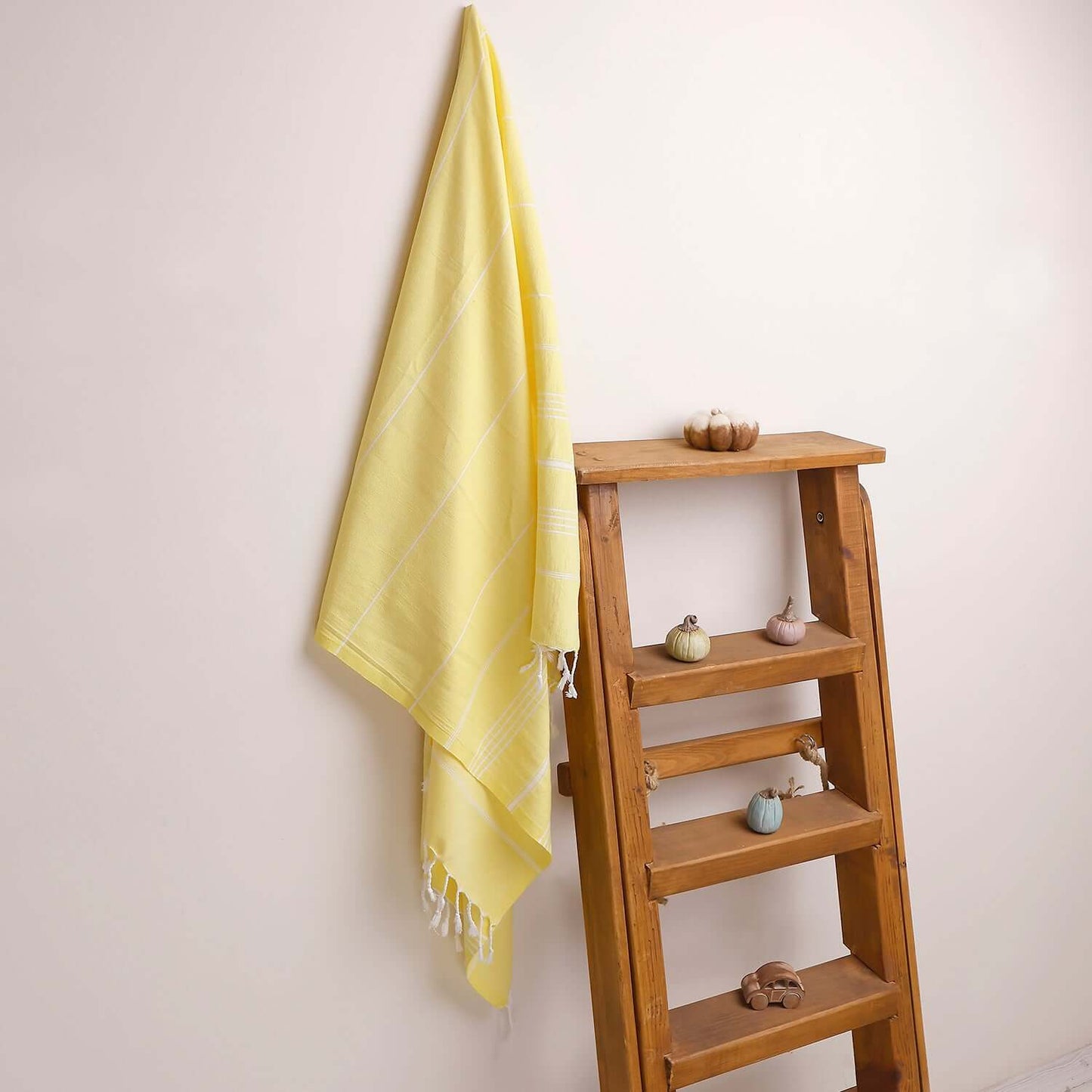 Loom Legacy yellow striped beach towel with tassels, draped over a wooden ladder beside small decorative items on the shelves.