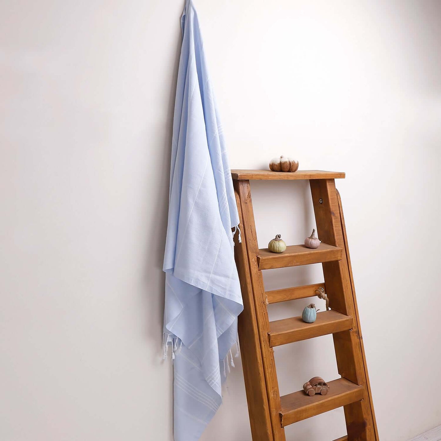 Loom Legacy light blue striped beach towel with tassels, draped over a wooden ladder beside small decorative items on the shelves.