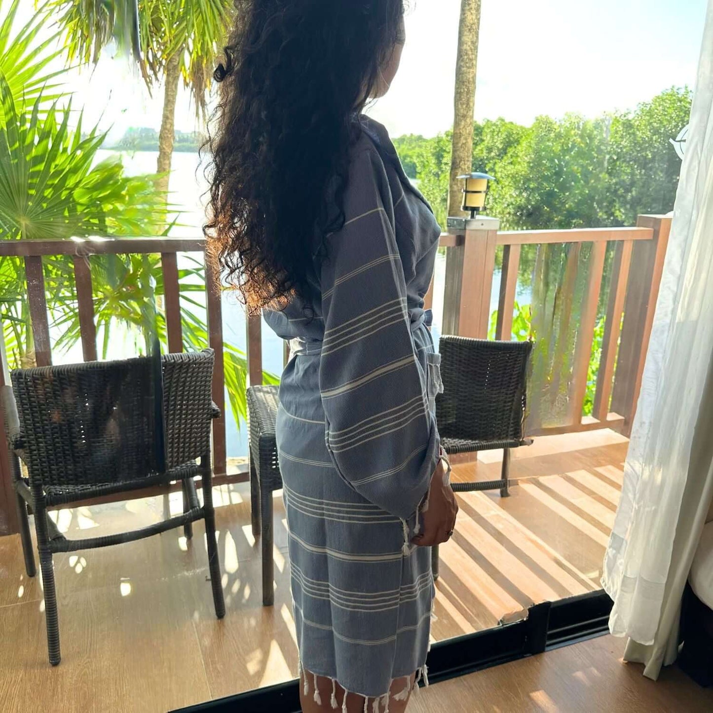 Woman wearing a blue xsmall/small 'The Loom Legacy' bathrobe, gazing at a serene lakeside view from a balcony surrounded by greenery.