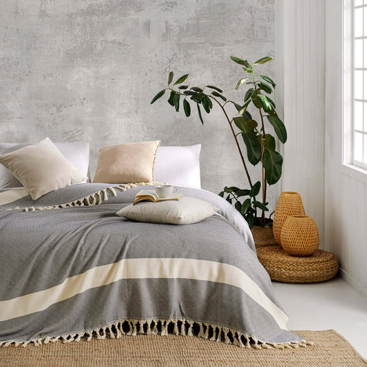 Loom Legacy grey and beige cotton blanket in a serene setting with white pillows, indoor plant, and woven accents.