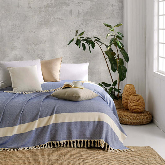 Loom Legacy blue and beige cotton blanket in a serene setting with white pillows, indoor plant, and woven accents.