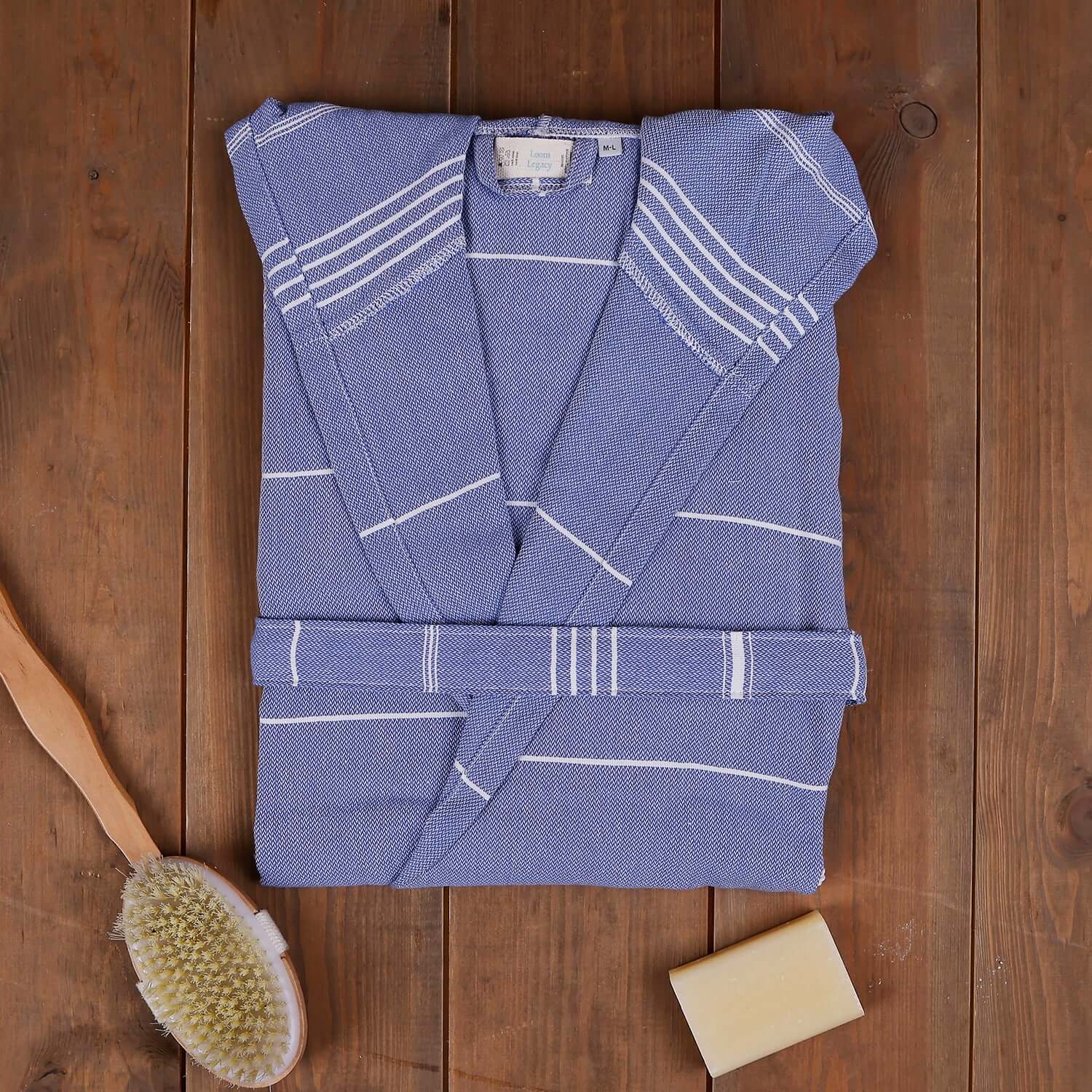 Blue xsmall/small 'The Loom Legacy' bathrobe with white patterns on a wooden surface, accompanied by a bristle brush and soap bar.