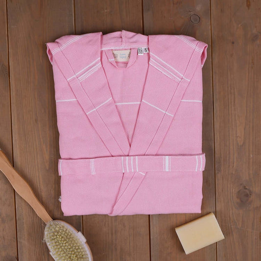 Pink xsmall/small 'The Loom Legacy' bathrobe with white patterns on a wooden surface, accompanied by a bristle brush and soap bar.