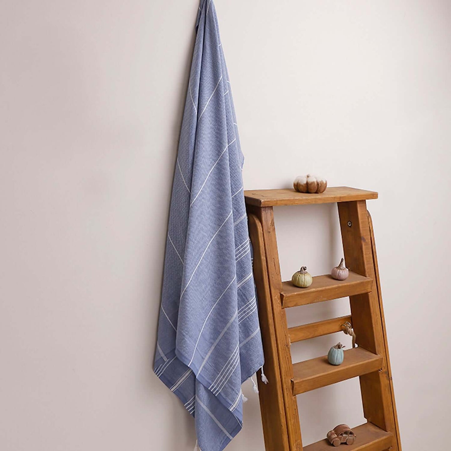 Loom Legacy dark blue striped beach towel with tassels, draped over a wooden ladder beside small decorative items on the shelves.