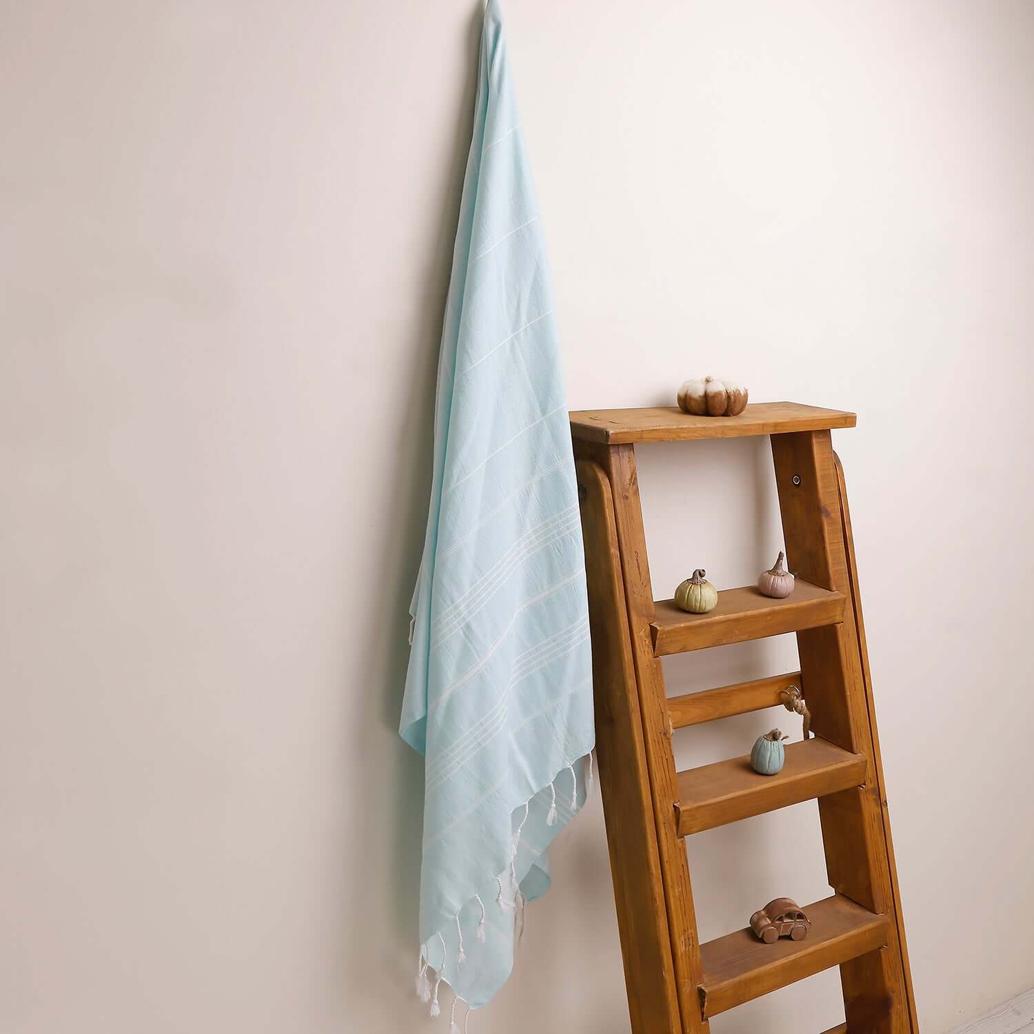 Loom Legacy aqua striped beach towel with tassels, draped over a wooden ladder beside small decorative items on the shelves.