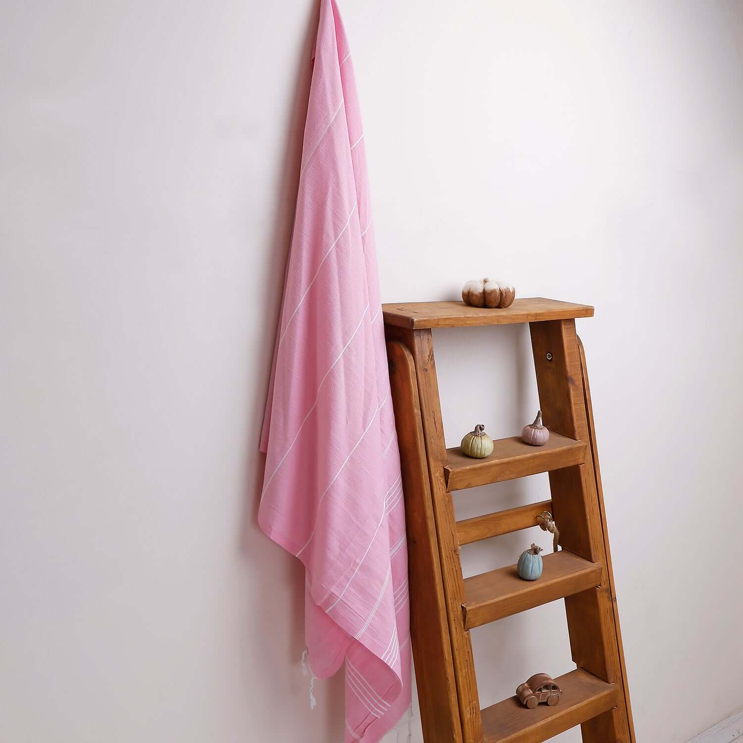 Loom Legacy pink striped beach towel with tassels, draped over a wooden ladder beside small decorative items on the shelves.